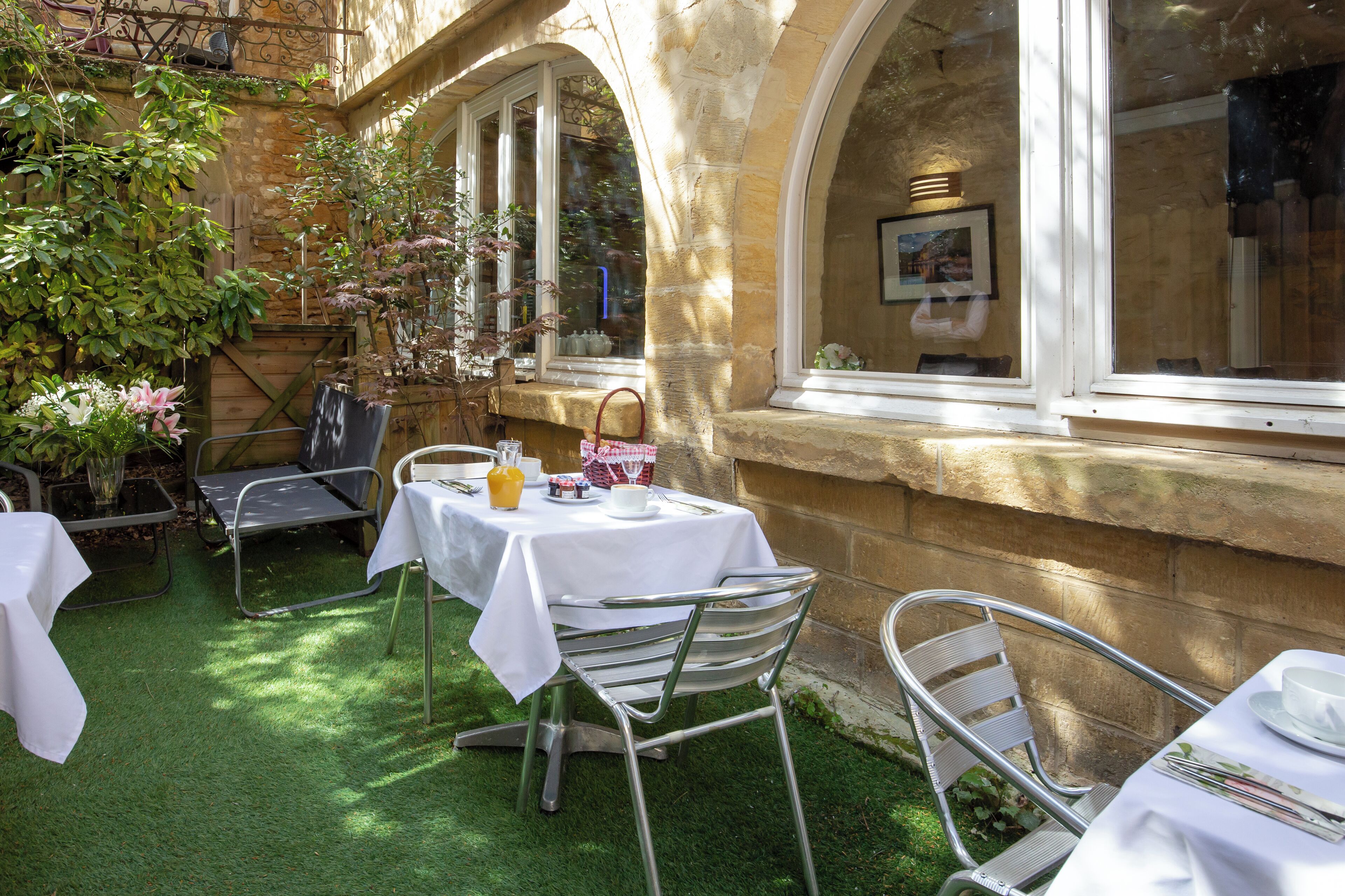 An outdoor patio with tables and chairs, surrounded by stone walls and windows.