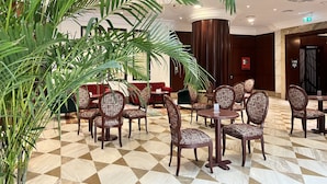 A lobby with round tables and chairs, a large potted plant, and a check-in counter. - City Seasons Suites (Dubai)