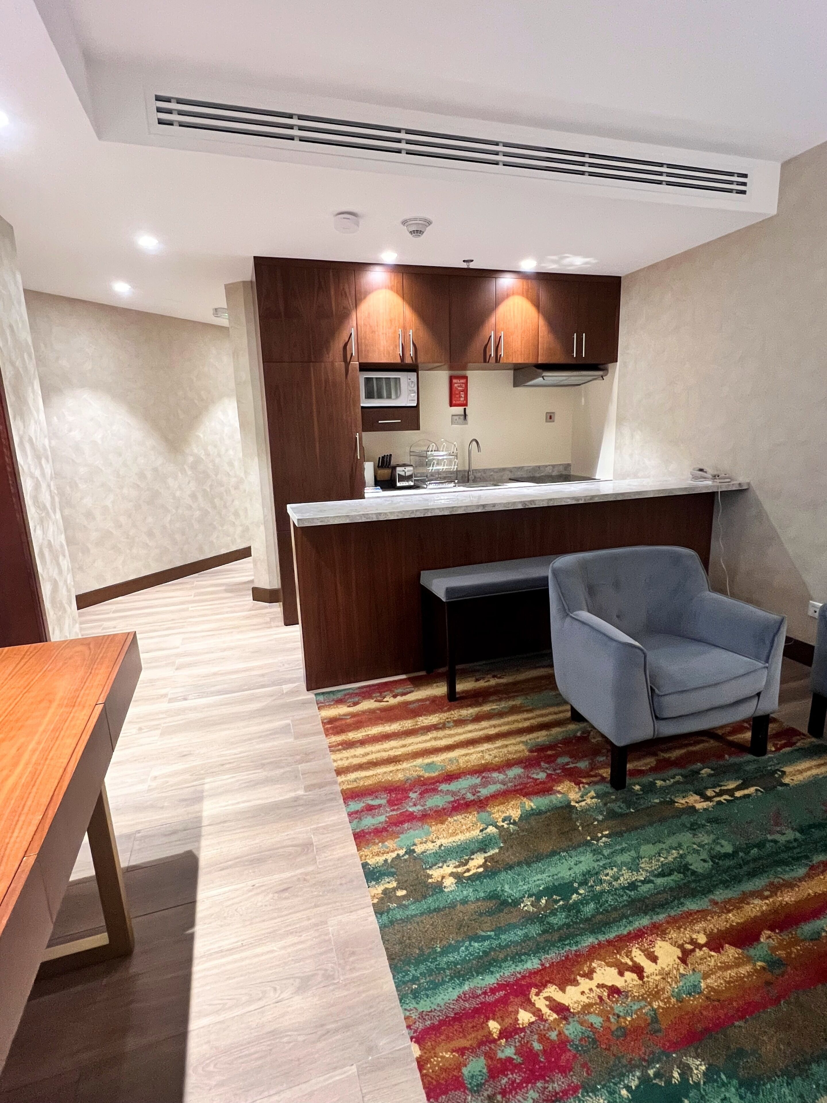 A compact kitchen with a microwave, sink, and wooden cabinets. There's a bench and a chair in the dining area.