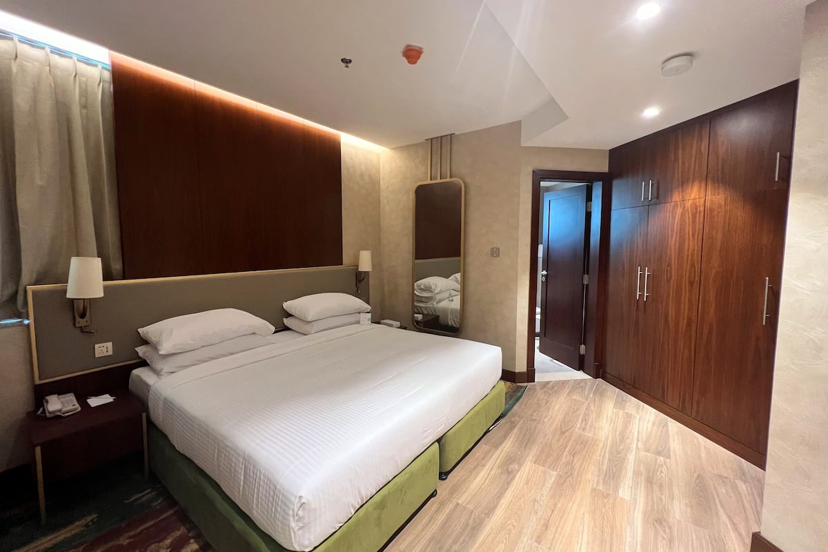 A hotel room with a large bed, bedside lamps, a mirror, a wardrobe, and a carpeted floor.