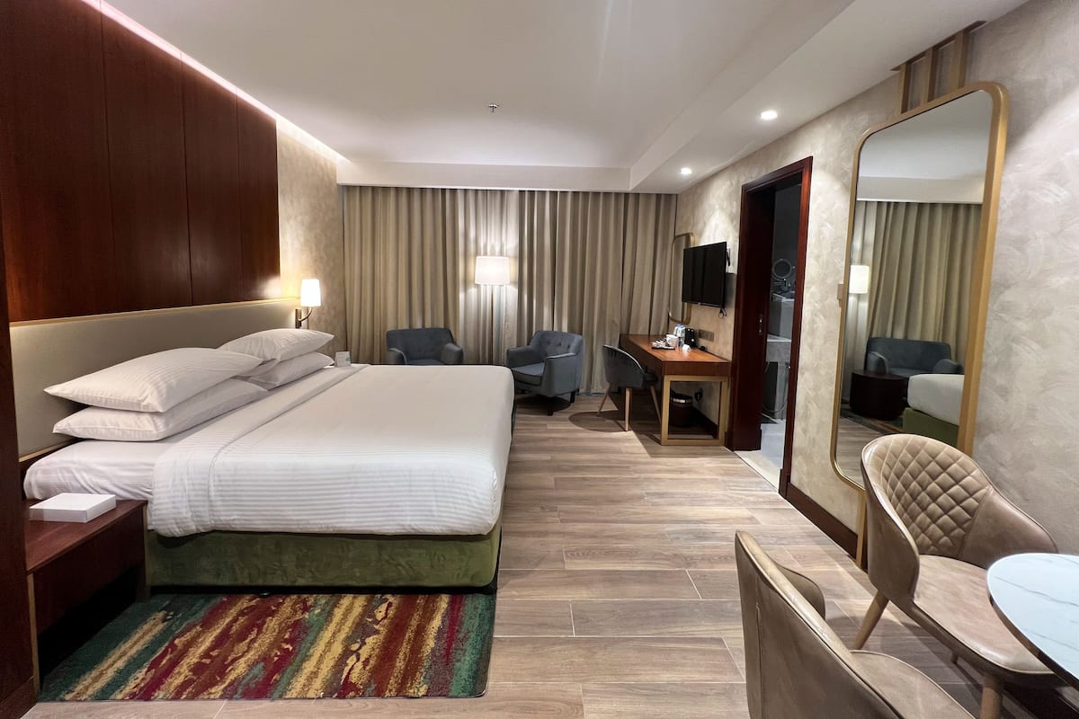 A hotel room with a large bed, a desk, two chairs, a mirror, and a TV.