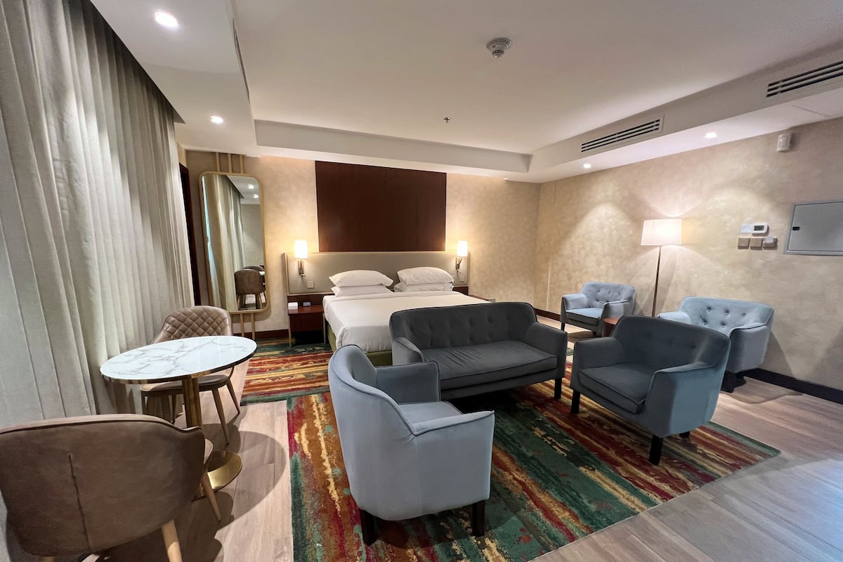 A hotel room with a bed, two armchairs, a sofa, a small table, and a mirror.