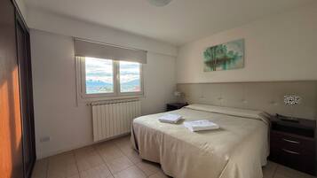 Une chambre à coucher avec un lit, un radiateur, une fenêtre donnant sur un beau paysage et un tableau accroché au mur.