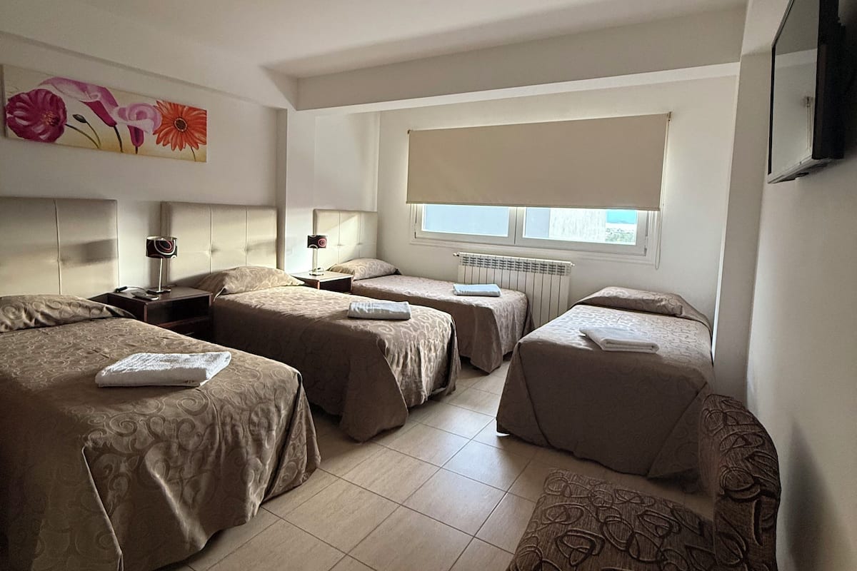 A hotel room with three beds, a chair, a TV, and a painting on the wall.