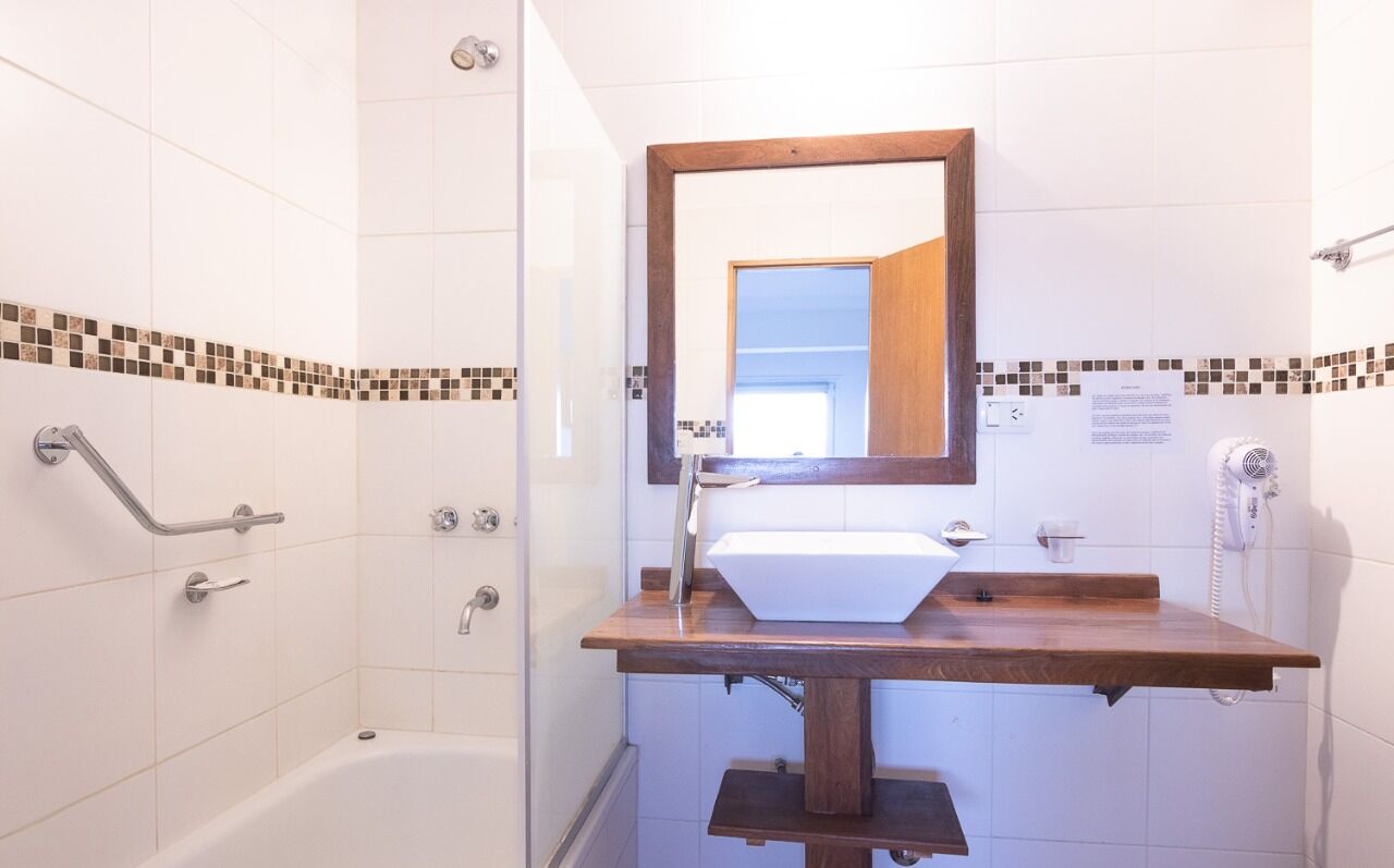 A bathroom with a white bathtub, a wooden vanity with a sink, a mirror, and a shower area with a grab bar.