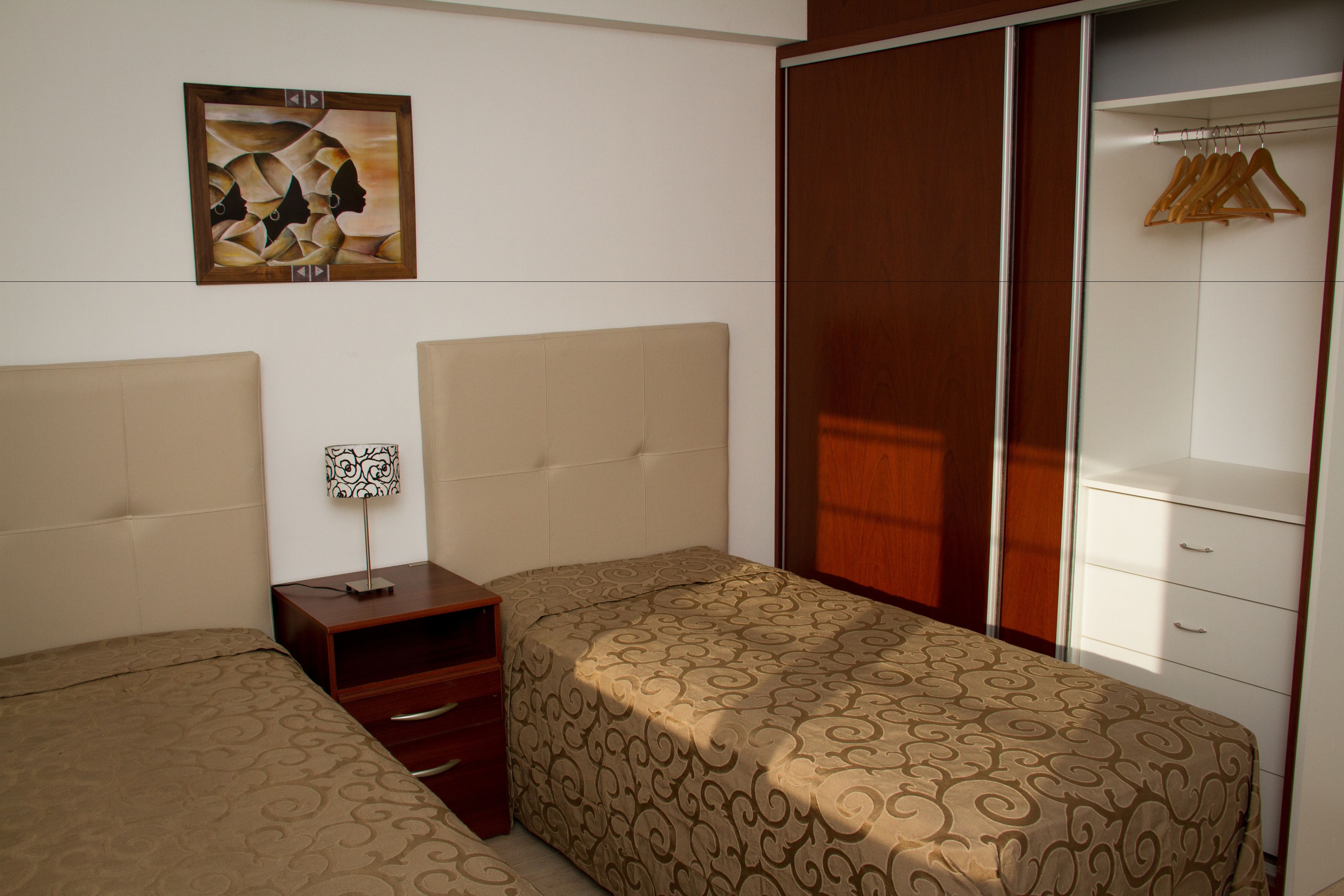 Quarto com duas camas, uma mesa de cabeceira, um guarda-roupa e um quadro na parede.