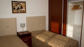 Quarto com duas camas, uma mesa de cabeceira, um guarda-roupa e um quadro na parede.