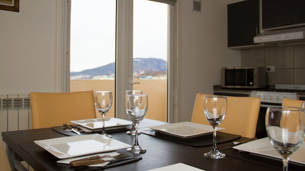 Een eettafel gedekt met borden, bestek en wijnglazen, in een kamer met uitzicht op bergen door grote ramen.