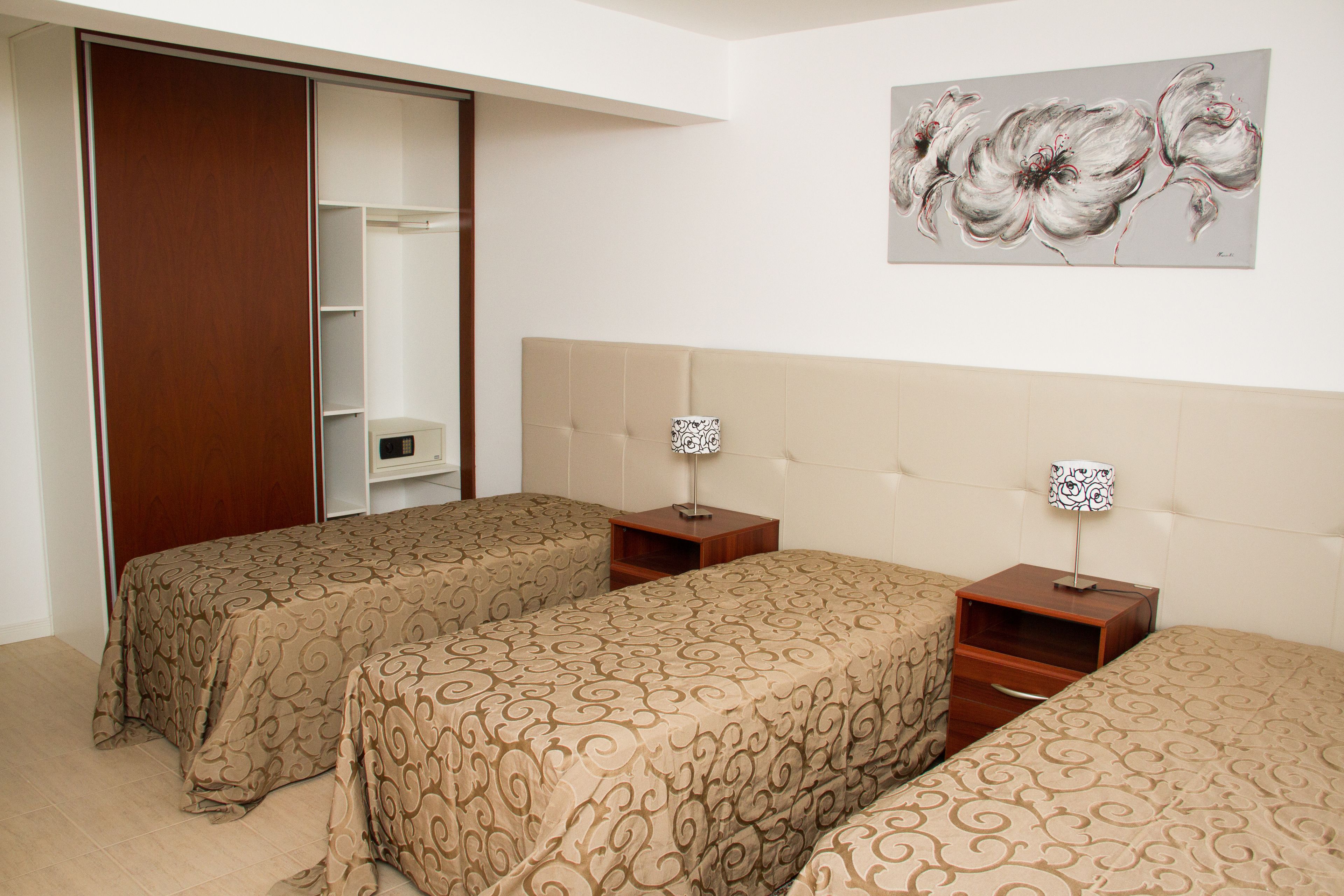Una habitación de hotel con dos camas, un armario, un cuadro en la pared y una mesita de noche con lámpara.