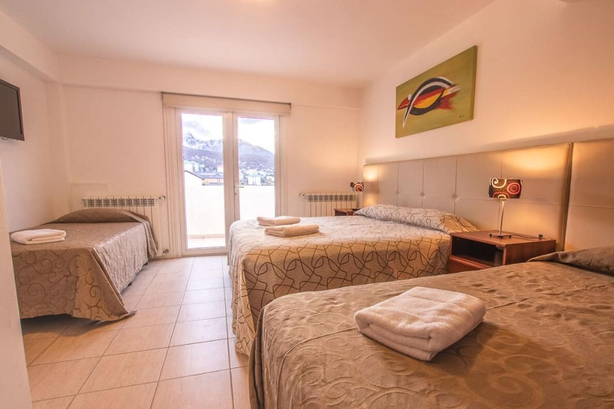 A hotel room with two beds, a large window, a painting, and a view of the mountains.