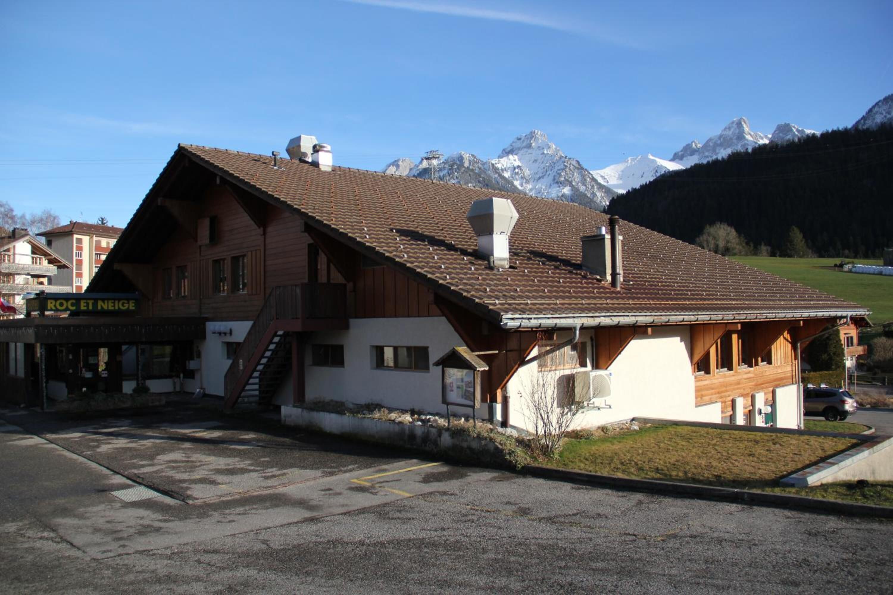 Un bâtiment en bois avec un toit en pente, une enseigne indiquant « ROC ET NEIGE », et un espace de stationnement devant.