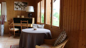Una habitación acogedora con una mesa redonda, dos sillas, una lámpara y una ventana que da a zonas verdes.