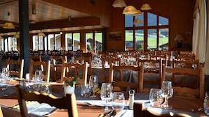 Un restaurante con interiores de madera, ventanas amplias y mesas dispuestas para comer.