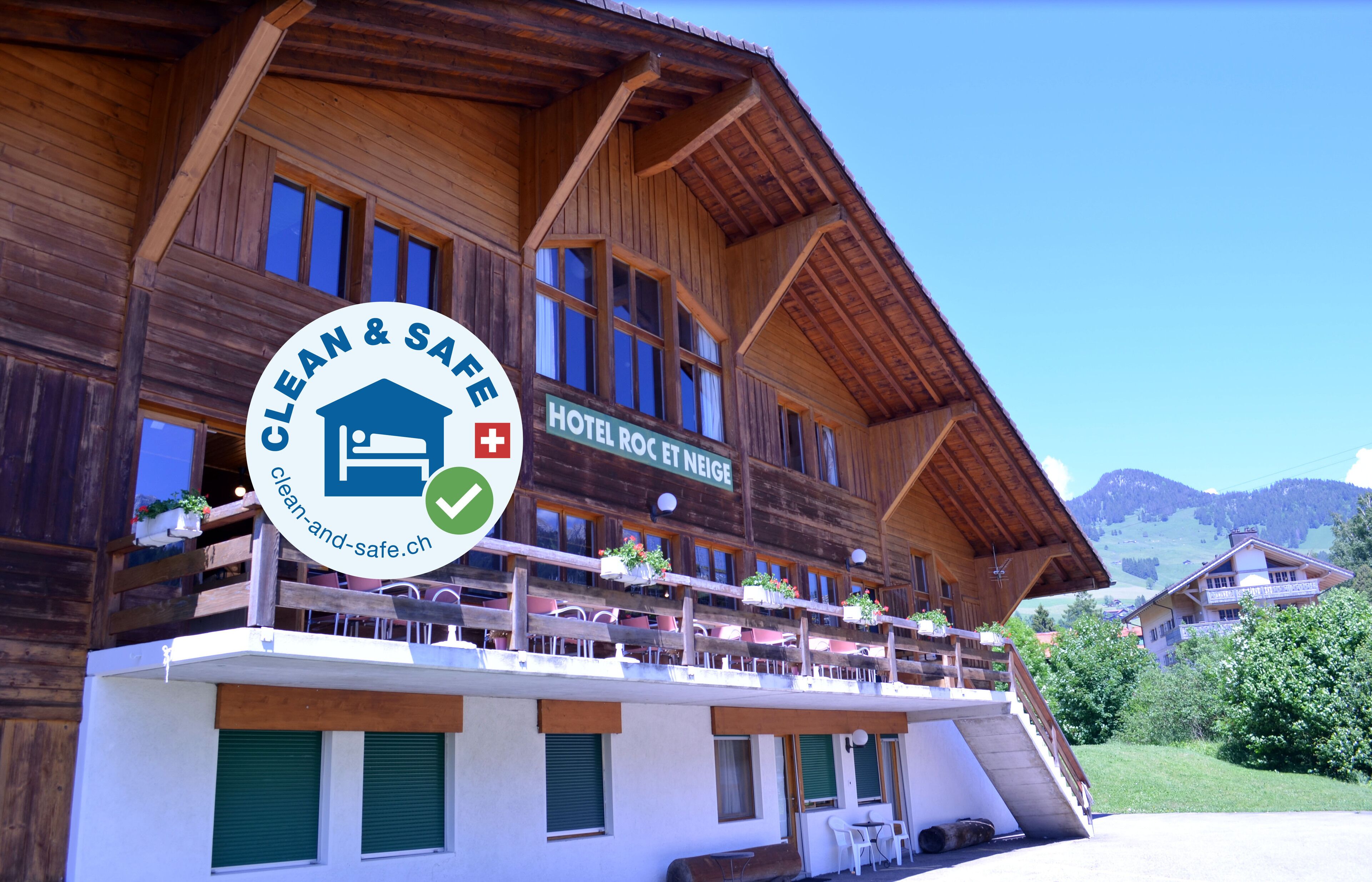 A wooden hotel with balconies, a sign indicating "Hotel Roc et Neige," and a logo for "Clean & Safe."
