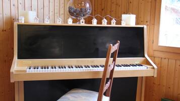 A piano with a wooden finish and a black backdrop, accompanied by a chair with a patterned cushion.