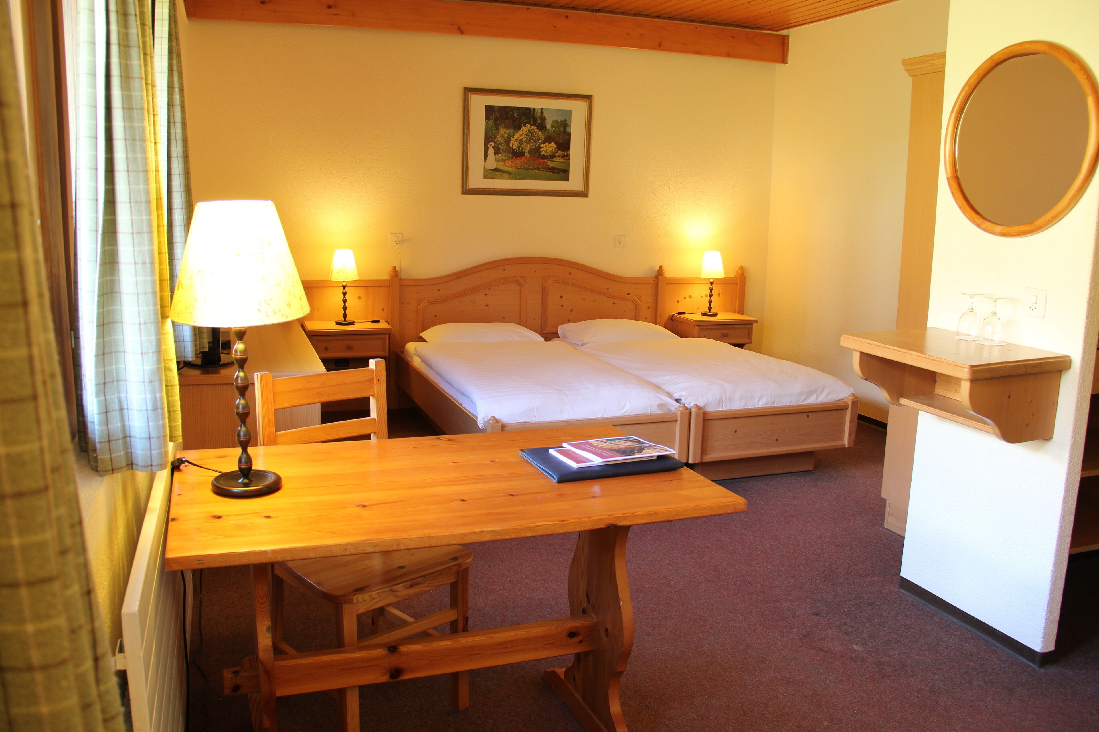 Um quarto com uma cama de madeira, duas mesas de cabeceira com luminárias, uma escrivaninha de madeira, uma cadeira e um espelho sobre um aparador.