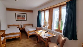 Una habitación con dos camas de madera, una mesa de madera con sillas, una ventana con cortinas y un cuadro en la pared.