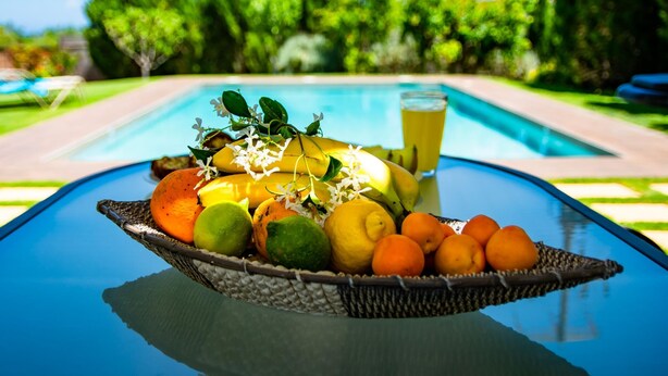 A fruit basket on a table with a pool and greenery in the background. - Villa Dimokratia (Platanias)