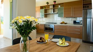 A modern kitchen with wooden cabinets, a stainless steel refrigerator, and a dining table set with food and a vase of flowers. - Villa Dimokratia (Platanias)