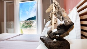A room with a bed, a wooden sculpture on a table, and a view of a mountain through a window. - Villa Dimokratia (Platanias)