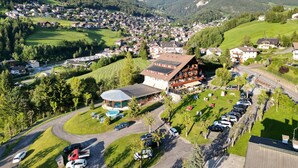 A mountain village with a prominent building featuring a sloped roof and a swimming pool. - Hotel Rodes (Castelrotto)