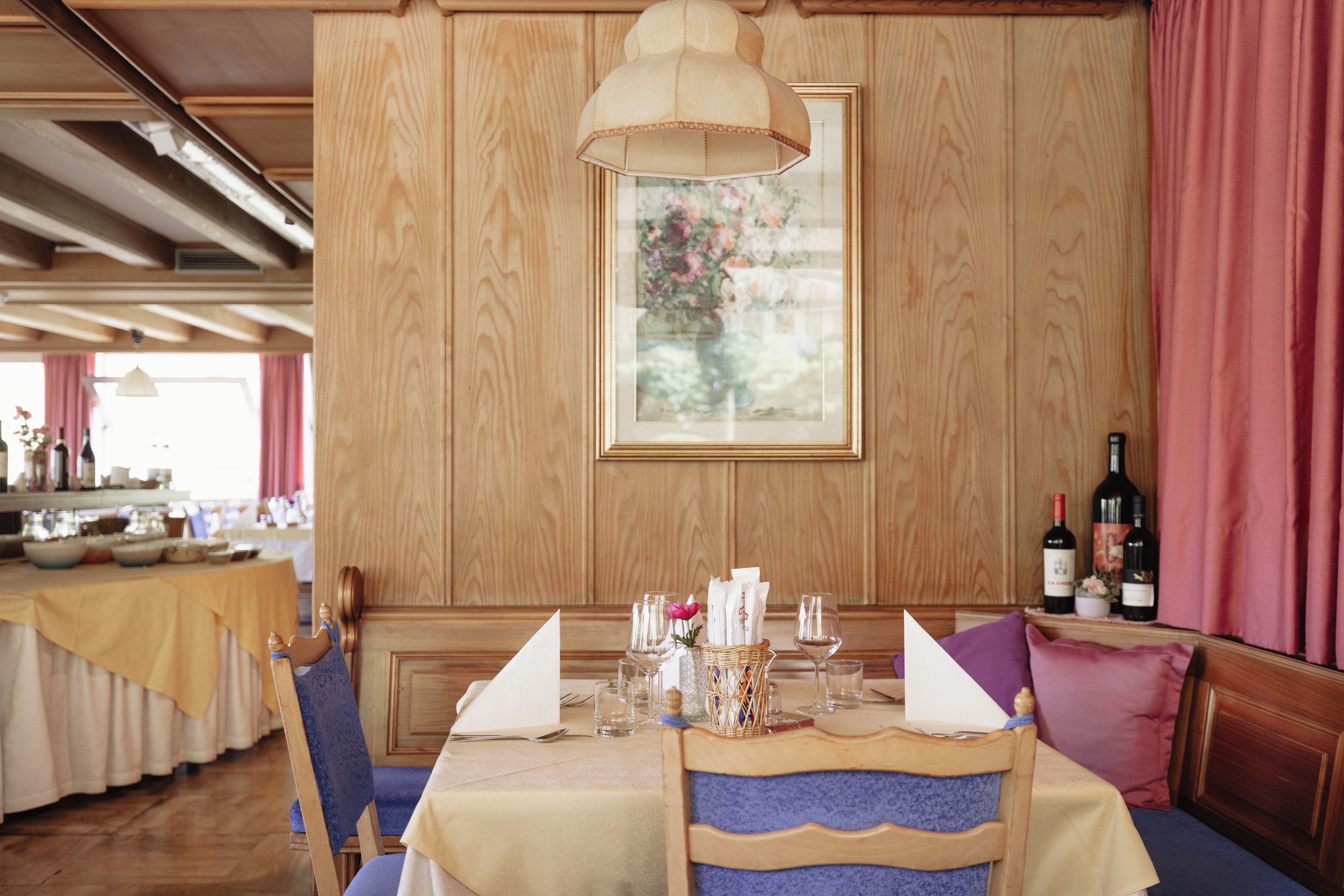 Un comedor con una mesa preparada para dos personas, una pared revestida de madera y una obra de arte floral enmarcada sobre la mesa.