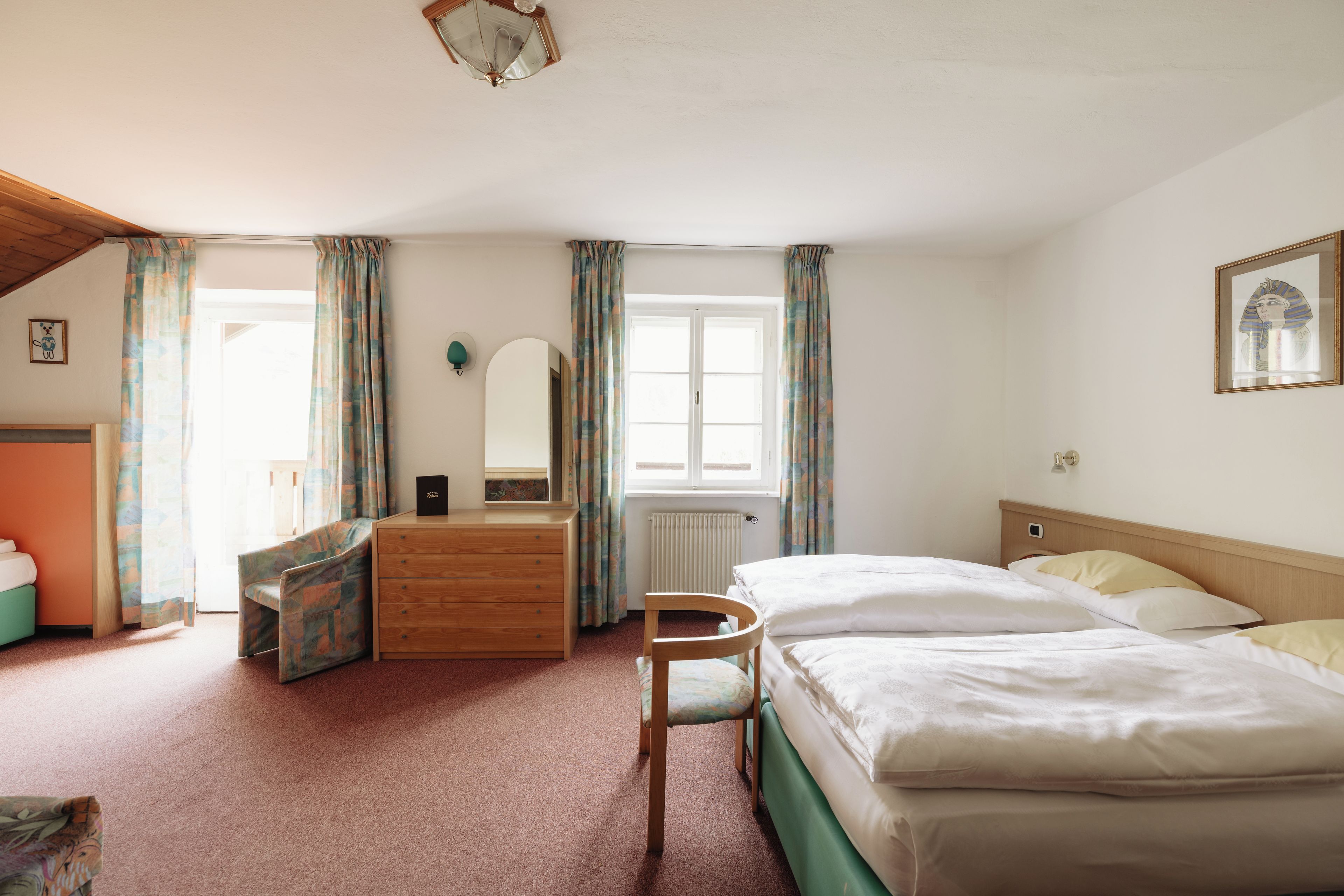A bedroom with a bed, a dresser, a chair, a mirror, and a window with curtains.