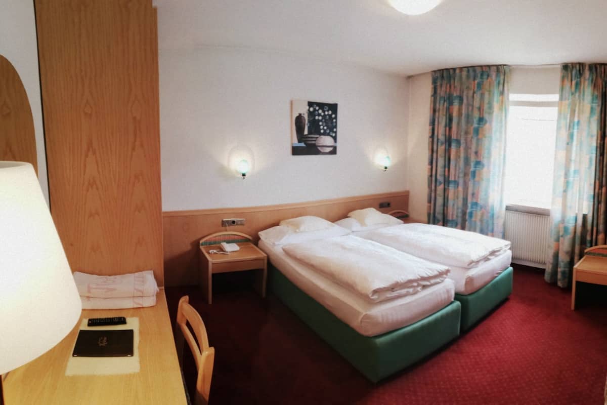 Habitación de hotel con cama doble, cama individual, sofá, televisor, lámpara, un cuadro y cortinas.