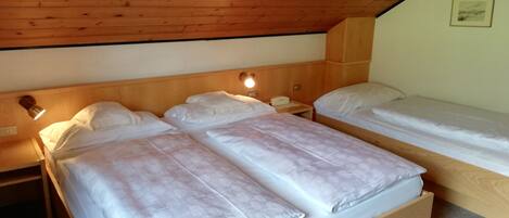 A room with two wooden beds, each with white bedding and a headboard. There is a nightstand with a lamp and a telephone on one side. The room has a sloped wooden ceiling and a framed picture on the wall.