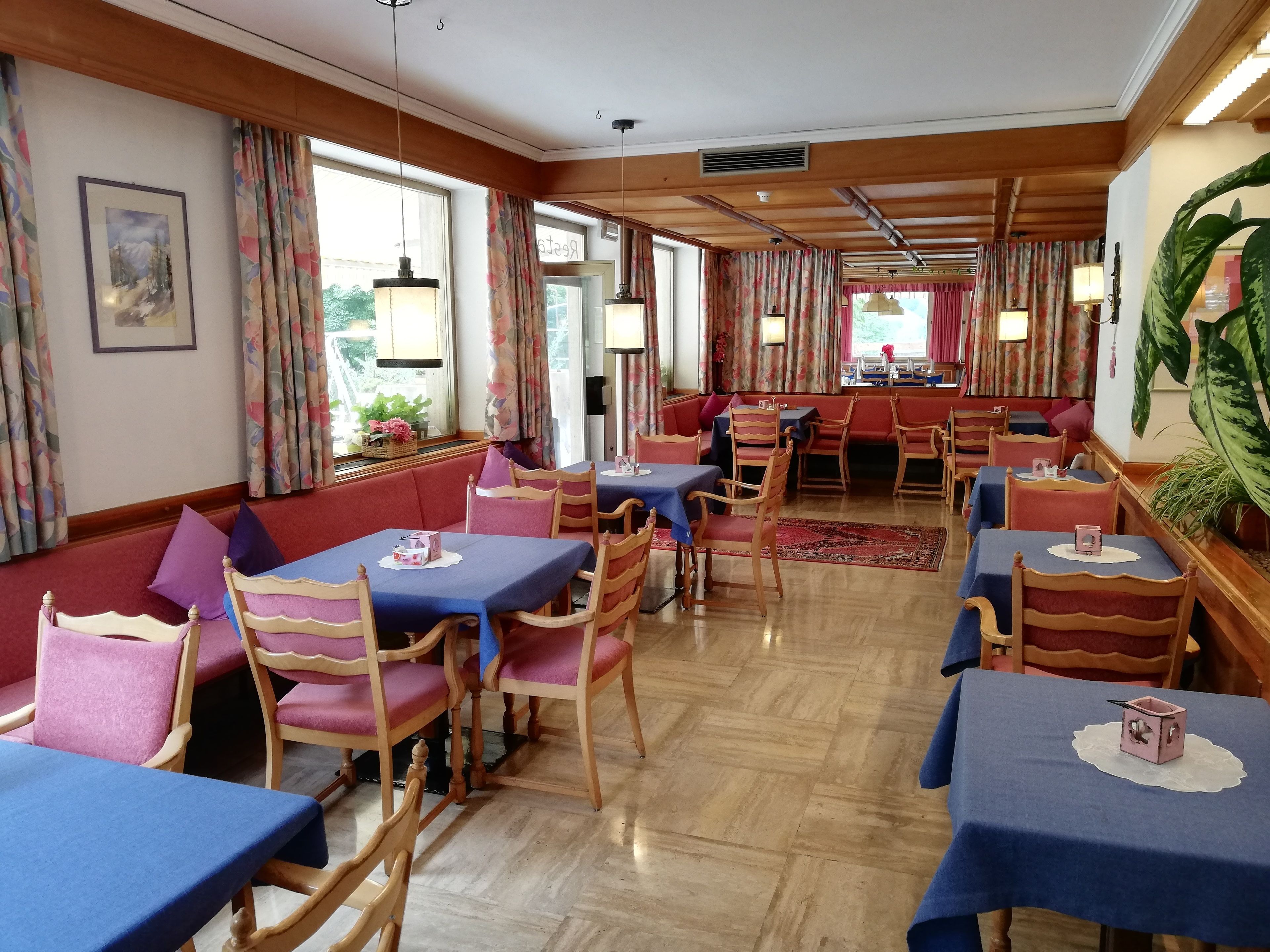 A restaurant with wooden tables and chairs, floral curtains, and a view of the outdoors.