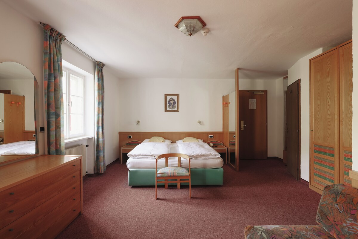 A hotel room with a bed, a chair, a dresser, a mirror, and a window with curtains.