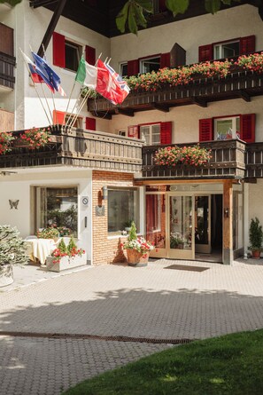 A hotel with a traditional European architectural style, featuring a balcony with flower boxes and multiple flags. - Hotel Rodes (Castelrotto)