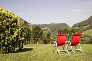 Two red lawn chairs facing a scenic view of a mountainous landscape with a clear sky. - Hotel Rodes (Castelrotto)
