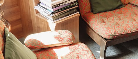 Ein Zimmer mit einem gemusterten Sessel, dazu passendem Hocker und einem Stapel Bücher auf einem kleinen Holztisch.
