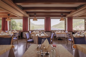 Un restaurante con mesas dispuestas para comer, ventanas amplias con cortinas y vistas a un valle.