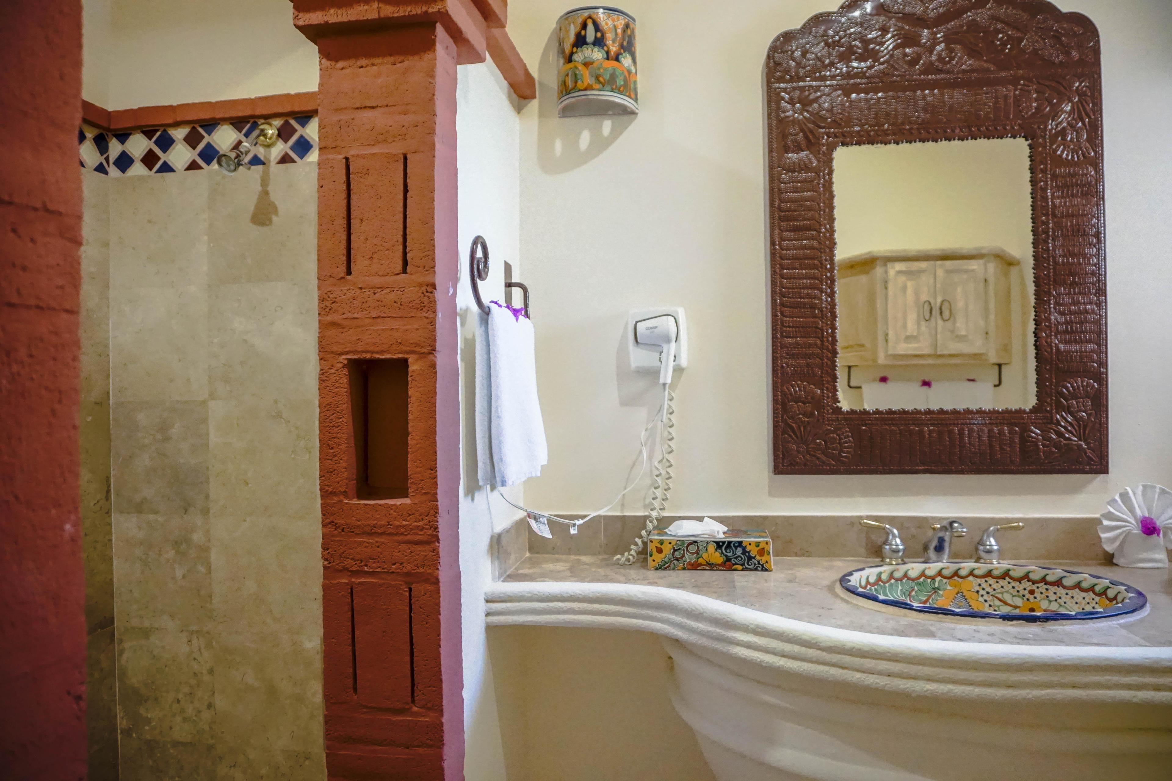 Un baño con ducha, un lavabo con pileta decorativa, un espejo con reflejo de un gabinete y un perchero para toallas.