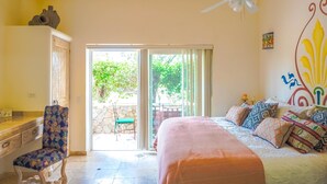 Quarto com cama, escrivaninha, cadeira, ventoinha no teto e vista para o exterior.