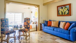 Uma sala de estar com um sofá azul, poltronas florais, uma mesa de centro e um ventilador de teto.