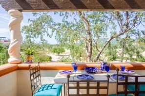 A terrace with a table set for dining, overlooking a scenic landscape with trees and hills. - KING BED CountryClub 1 Bedroom Apartment By Senstay (Cabo San Lucas)