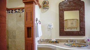 Casa de banho com chuveiro, pia com bacia decorativa, espelho com reflexo de armário e um porta-toalhas.