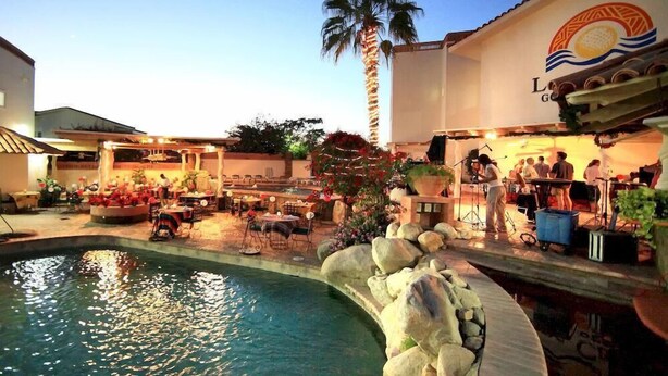 Area piscina con palma, posti a sedere all'aperto e un palco per musica dal vivo.
