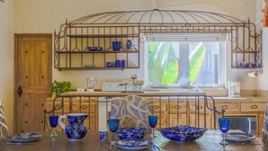 Una cucina con una porta di legno, una finestra che si affaccia su un verdeggiante fogliame e un espositore metallico con stoviglie azzurre.