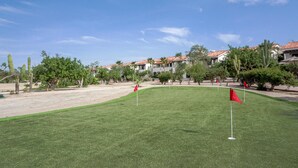 A well-maintained golf course with red flags marking the holes, surrounded by cacti and trees, and buildings with red-tiled roofs in the background. - 7BED Country Club 2 3 Bedroom Apartment By Senstay (Cabo San Lucas)