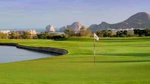 A golf course with a water hazard, a flagstick, and a mountainous backdrop.
