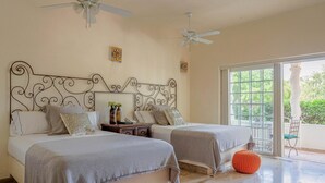 A bedroom with two beds, a ceiling fan, and a large window with a view of greenery.