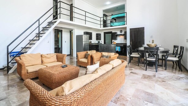 Uma sala de estar ampla com teto alto, escada e área de cozinha.