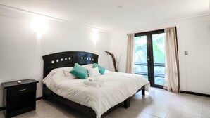 Quarto com cama, mesa de cabeceira, porta de correr para uma varanda e luminária no teto.