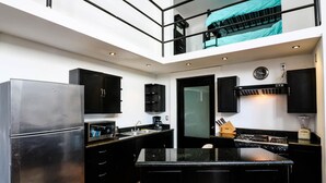 Cozinha moderna com armários pretos, geladeira de aço inoxidável, micro-ondas, fogão e pia.