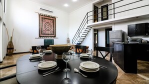 Uma área de refeições com uma mesa redonda posta para seis pessoas, uma tigela decorativa grande e uma escada que leva a um andar superior.