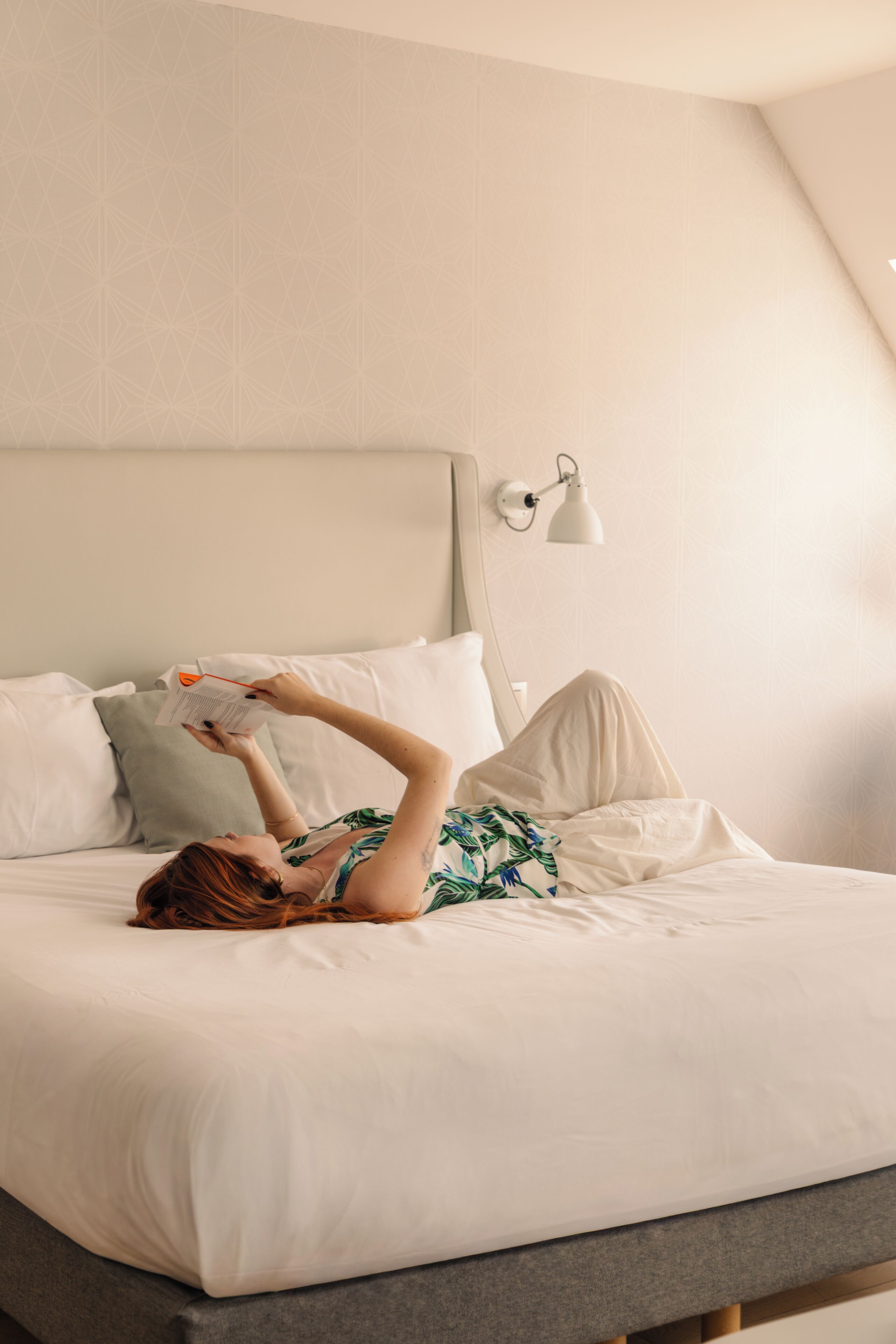 A bed with white linens, a person lying on it, and a wall-mounted lamp.